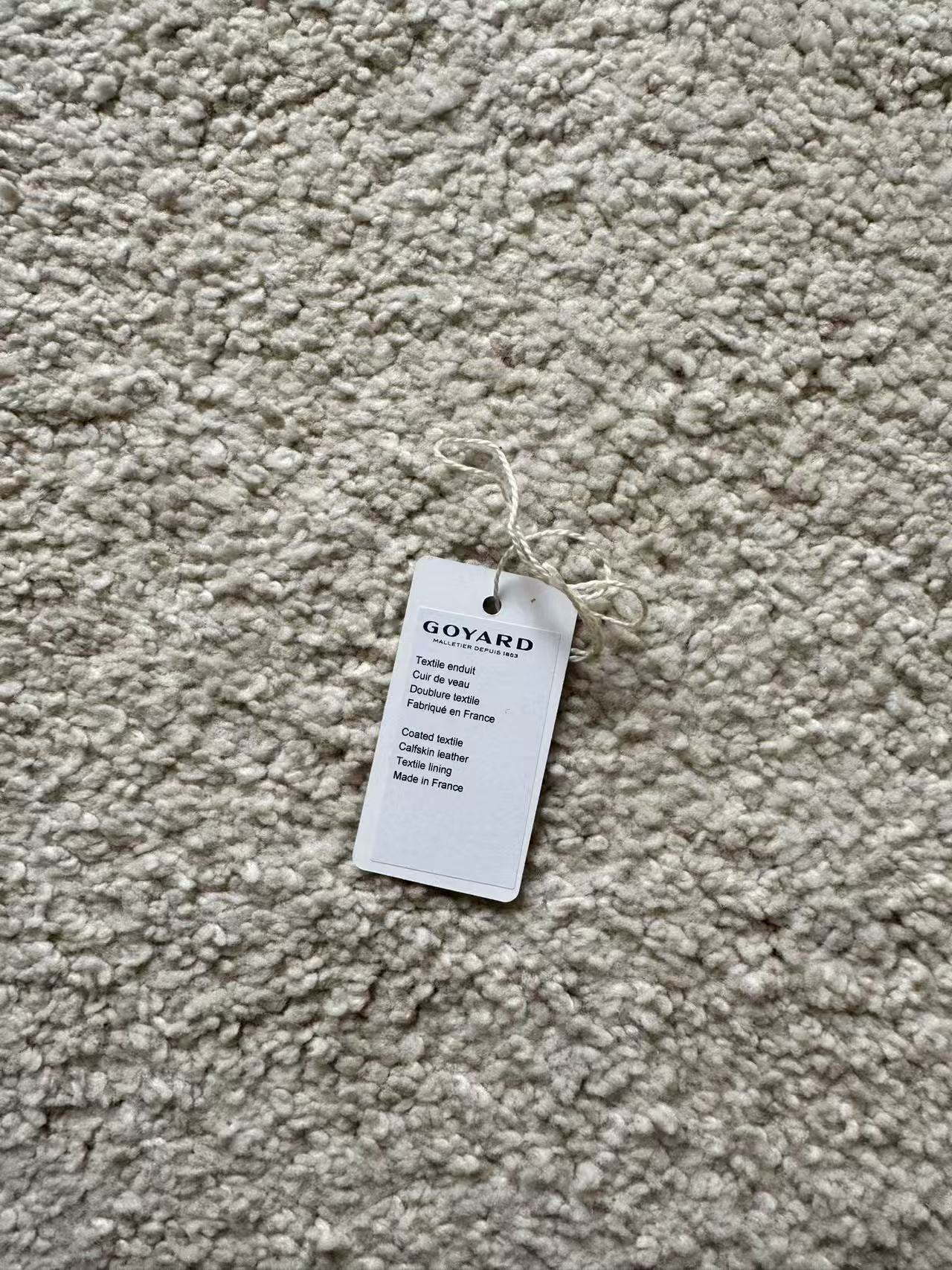 Goyard tag on a textured beige fabric surface