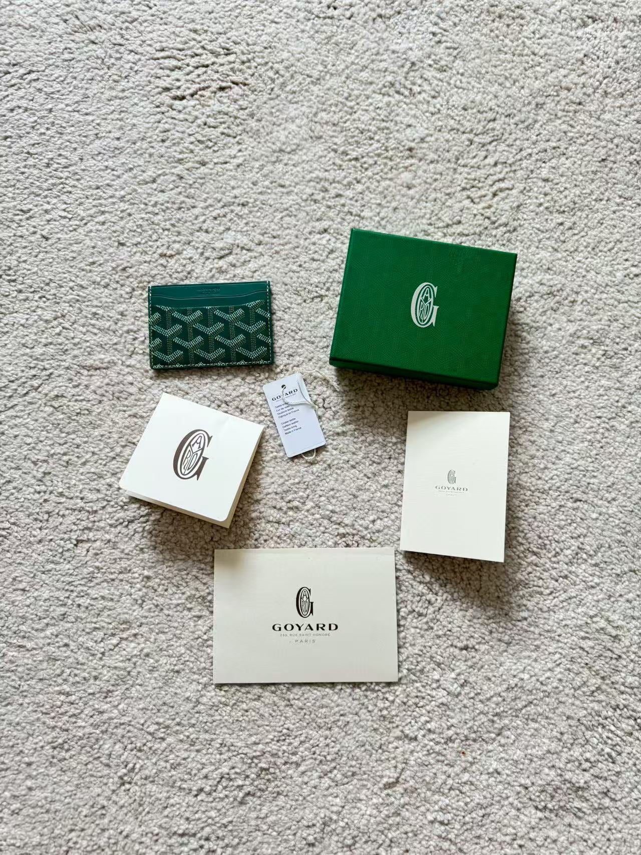Goyard packaging items including a green box, card, and paper on a textured surface