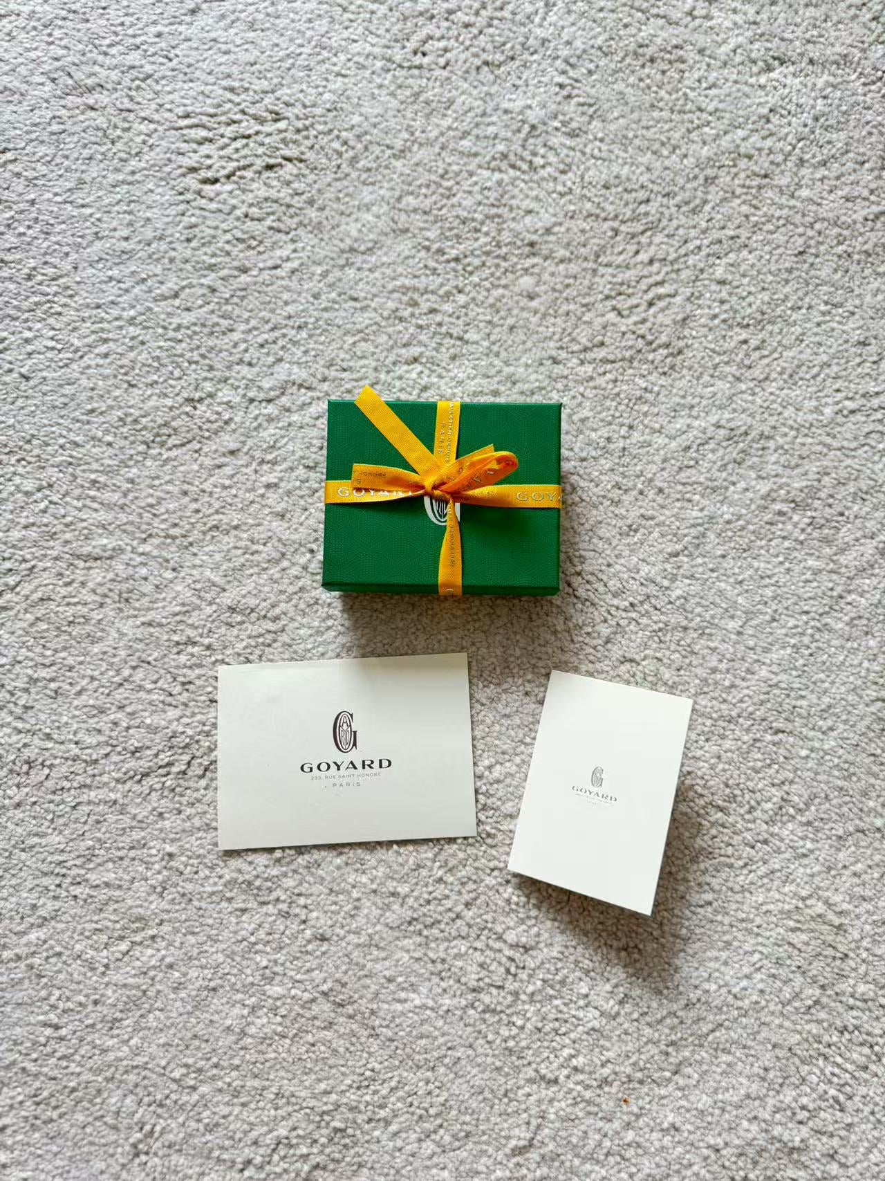 Green gift box with a yellow ribbon and two Goyard cards on a gray surface