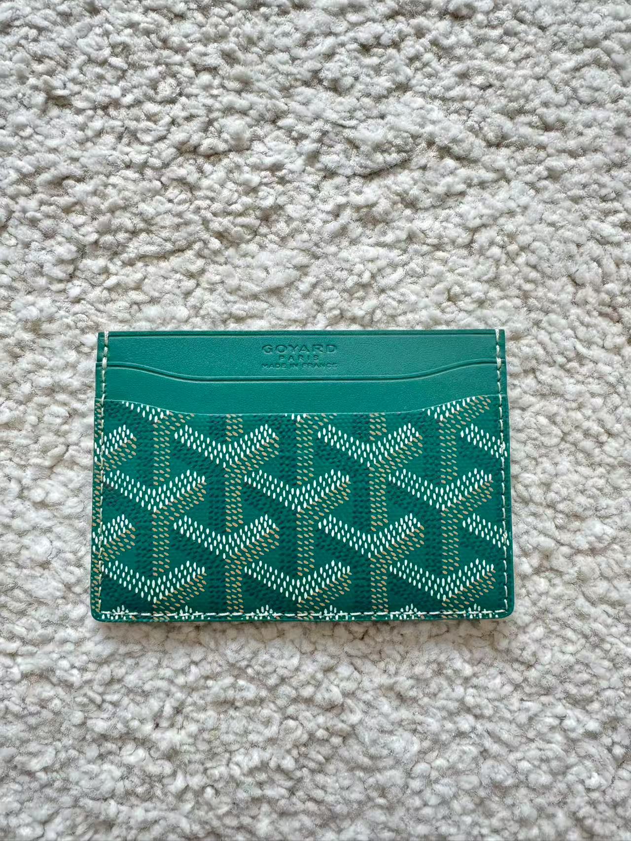 Green cardholder with geometric pattern on a textured beige surface
