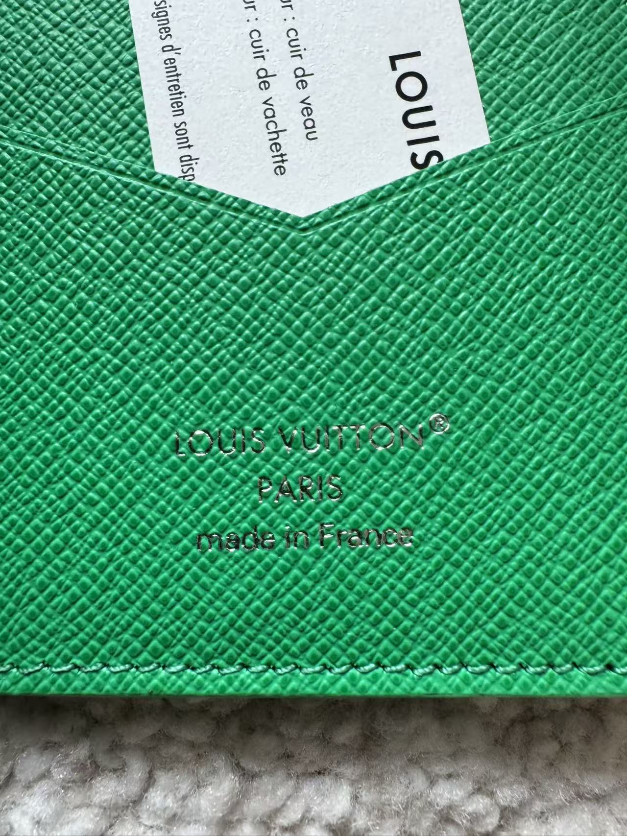 Close-up of a green Louis Vuitton wallet with branding details.