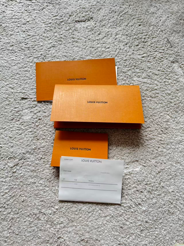 Louis Vuitton packaging including orange boxes and a card on a textured gray surface