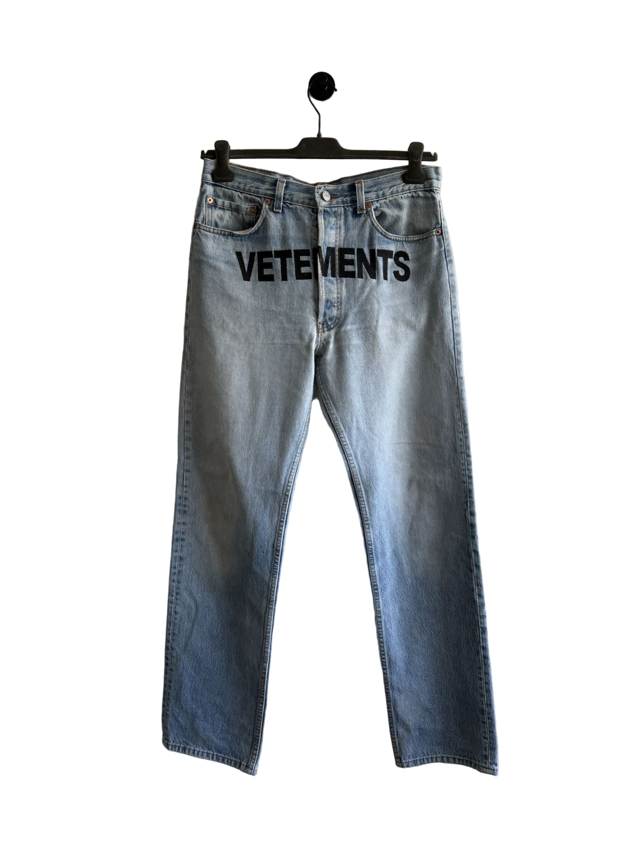 Blue jeans with 'VETEMENTS' branding on a hanger against a white wall