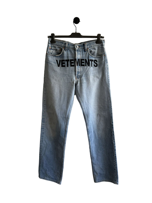 Blue jeans with 'VETEMENTS' branding on a hanger against a white wall